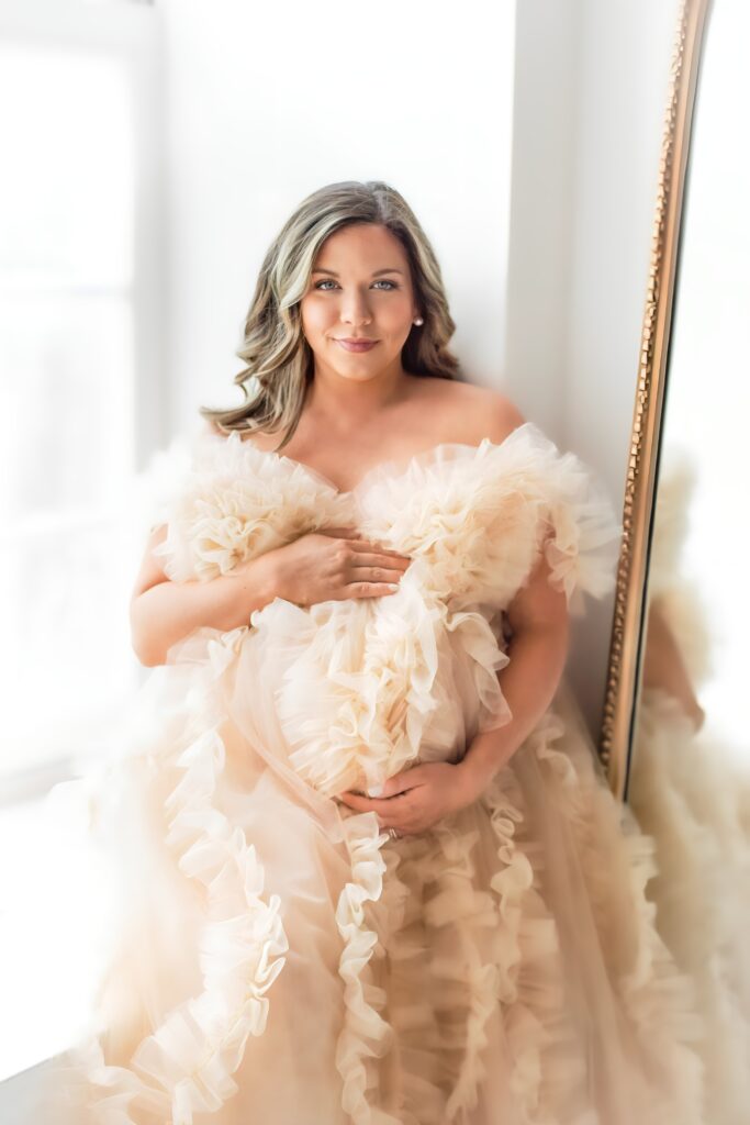 Studio maternity session with expectant mother in a flowy dress, standing in soft natural light.