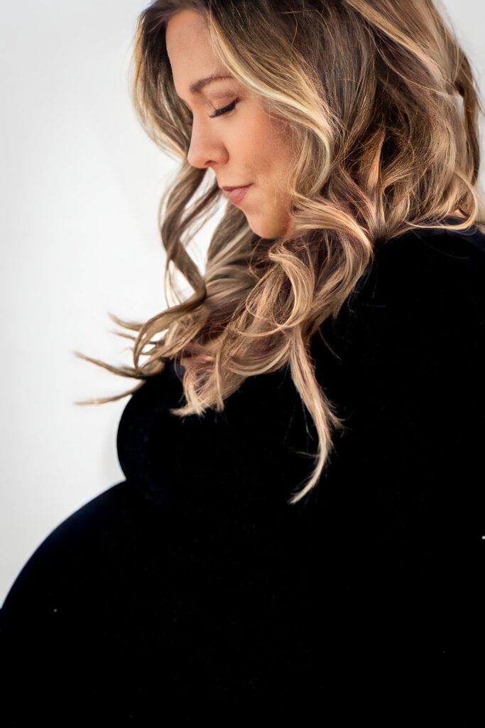 Studio maternity session with mother wearing a fitted black dress, showcasing the beauty of early motherhood.