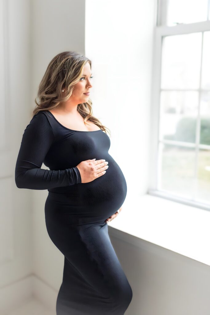 Intimate studio maternity session highlighting the expectant mom in a sleek black dress, embracing the journey of pregnancy.